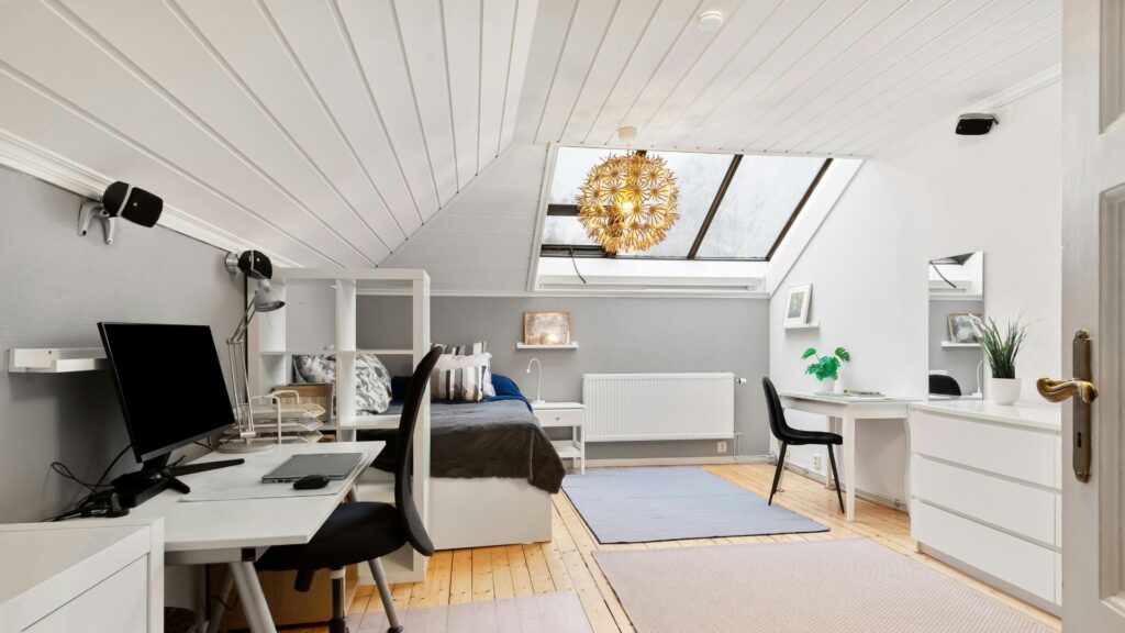 Finished attic bedroom and home office with sloped ceiling, skylight, desk, bed, and wood flooring.