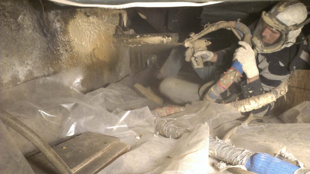Worker spraying insulation into crawl space.