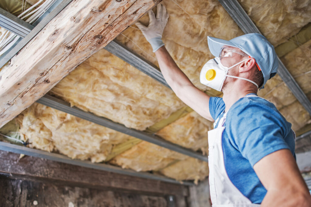 Installer checks ceiling batt insulation while wearing mask and goggles