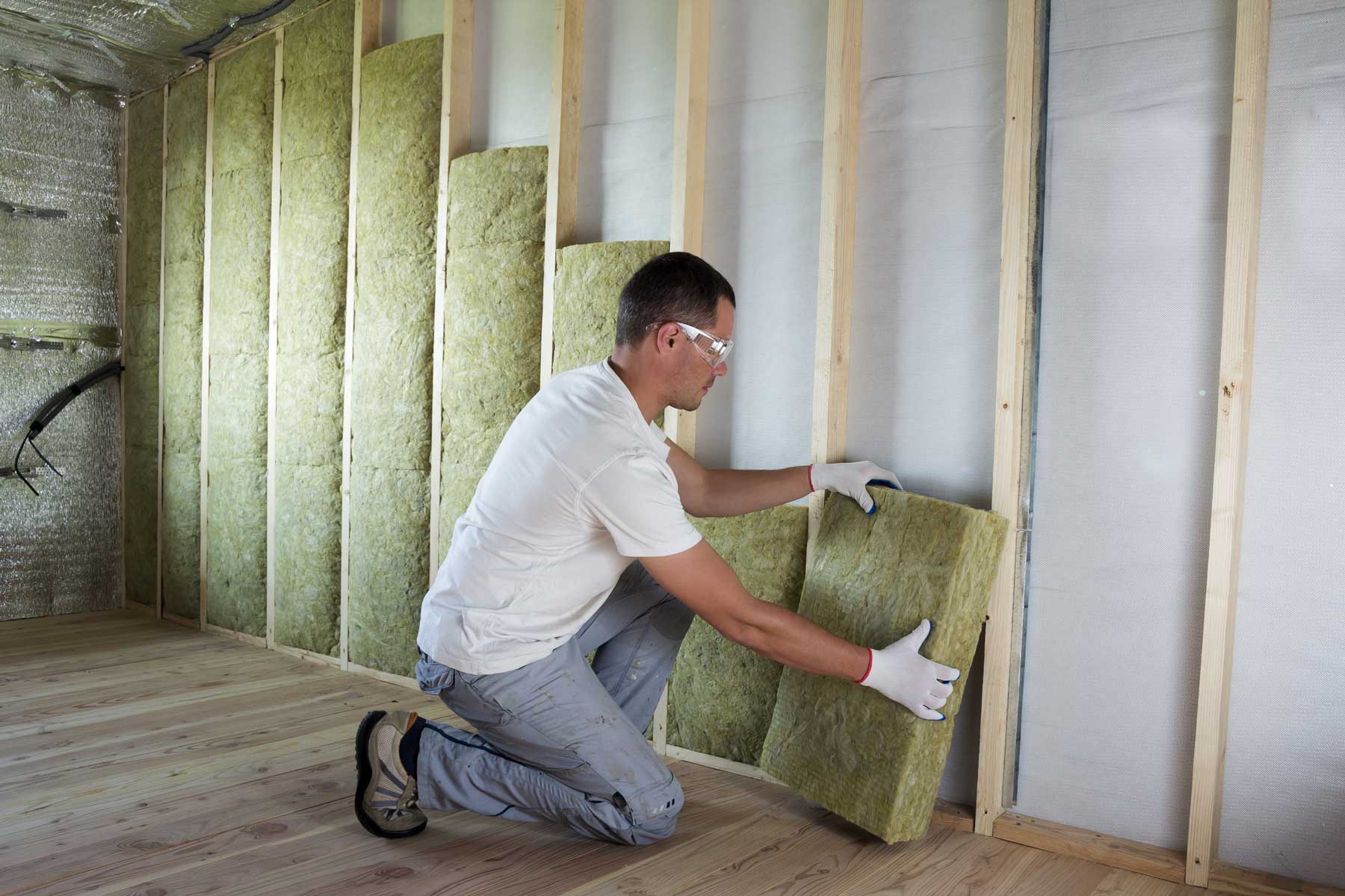 Installer fitting fibreglass batt insulation in a framed wall